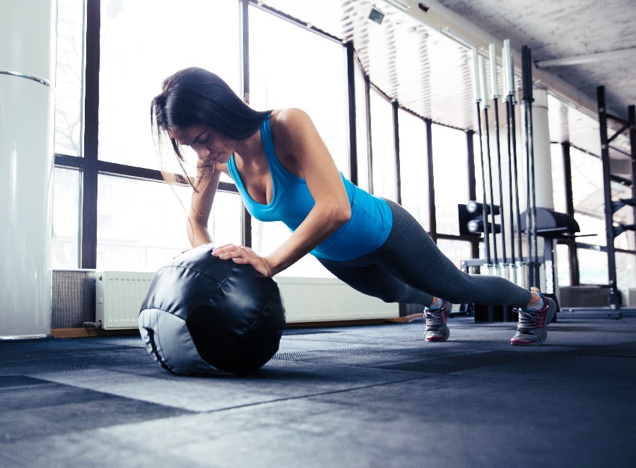 Eine Frau macht Liegestützen auf einem Medizinball im Fitnessstudio.